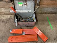 Overall view of the assortment showing orange Stihl plastic chain file guides and a metal toolbox containing various metal tools.