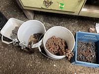 Three containers with assorted metal chains of varying thickness and lengths; two white buckets and one blue crate on ground.