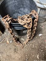 Rusty heavy-duty tractor tire chain coiled in a black container sitting on dirt floor.