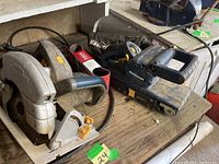 Side angle view showing the circular saw and belt sander on a wooden surface with visible power cords.