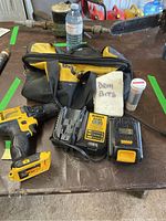 DeWalt cordless drill driver with battery attached, 2 batteries, chargers, drill bits container, and carrying bag on a table.