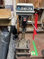 Front view of the Delta drill press showing the power switch, crank handle, and base with work table.