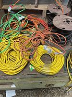 Various electric cords in yellow, orange, green colors coiled and some tangled on a table with some wire spools in the background.