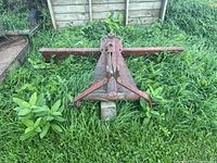 Overview of red-painted grader blade attachment lying in grass, showing full length blade and A-frame support