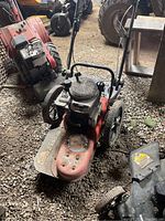Full view of red Briggs & Stratton push mower with deck, wheels, and handle in storage area