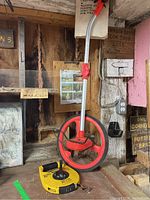 Full view of measuring wheel and tape on a workshop table, showing scale and setup.
