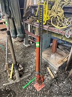Full view of the farm jack standing upright on gravel with surrounding tools and ropes on a shelf.
