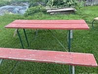 Full view of one picnic table showing red wooden top and attached bench on grass