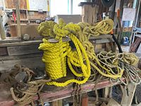 Photo showing assortment of ropes on wooden beam, including yellow synthetic rope coiled tightly and various brown natural fiber ropes coiled or loosely arranged.