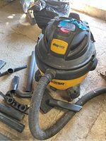 Overall image showing yellow and black Shop Vac Ultra vacuum cleaner with attached hose and several loose black plastic accessories on concrete floor.