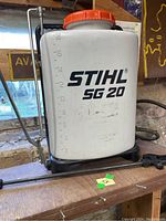 Front view of STIHL SG 20 plastic backpack sprayer showing volume markings and orange lid on white tank.