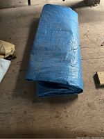 Folded large blue tarp showing creases and dirt marks on wooden floor