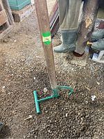 Full view of Timber Jack log roller/grabber tool standing on gravel ground showing wooden handle and green metal roller bar.