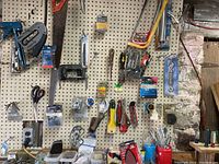 Photo showing pegboard with hanging hand saws, staplers, screwdrivers, scissors and various hand tools