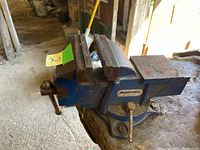 Side angle of blue Mastercraft metal vise mounted on a workbench, showing the full body and jaws.