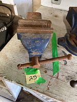 Blue metal vise showing rust on jaws and handle, placed on wooden table