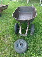 Front view of the wheelbarrow showing metal tub, two mounted tires, and extra tire on grass.