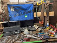 Wide photo showing tools spread on workbench with wrench set in blue pouch hanging in background, Old Pal toolbox, hammers, saws, and various hand tools.