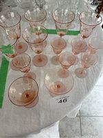 Top-down view showing 13 etched blush pink glasses and dessert cups arranged on a white cloth.