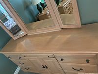 Front view of light wood dresser with multiple drawers and central cabinet under large tri-fold mirror