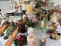 Wide shot showing assortment of candles, brass and glass candle holders, pink salt candle holder, carved angel wall hangings, and small holiday-themed decor on table.