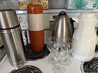 Wide view showing all items in the coffee set on stove and counter including kettle, carafe, vacuum bottles, and Irish Coffee glasses