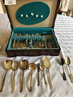 Silver flatware set arranged inside blue velvet-lined wooden case and additional large serving utensils in front