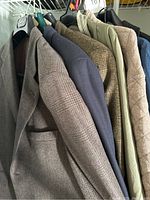 Photo showing six men's blazers and jackets on hangers in muted colors of brown, navy, tan, and beige.