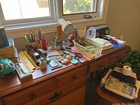 Desk with assorted office supplies including desk lamp, scissors, glue, rulers, pens, stapler, tape dispenser, plastic trays, papers, and a small globe-shaped object.