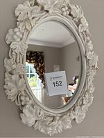 Full view of oval mirror with white plaster frame decorated with leaves and grapes.