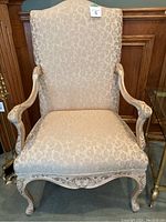 Front view of one upholstered Queen Anne style armchair showing beige fabric with floral pattern and carved wooden arms and legs.