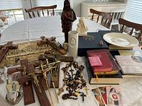 Overview of table with crucifixes, rosaries, statues, books, vases and plates