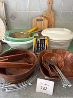 Photo of entire lot showing wooden salad bowls with matching tongs, small wooden bowls, white plastic salad spinner, green and white strainers, stainless steel sieve, nutcracker set, wooden cutting boards, and yellow mandolin slicer.