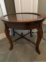 Full view of the oval wooden side table showing the removable glass top and curved legs with cross supports.