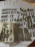 Overview of silverware utensils arranged on a round table including forks, knives, spoons and serving utensils with white plastic organizer tray.