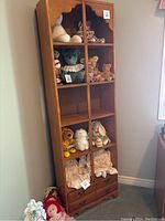 Full front view of the tall library showing eight shelving cubbies with various stuffed toys inside and two bottom drawers, wood tone medium color.
