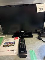 Full view of the RCA 19-inch LED TV, remote control, and part of the user manual placed beside the TV.