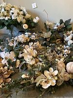 Various white faux flowers and green foliage arranged in bunches and loose stems on a surface.