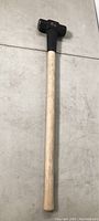 Full view of sledge hammer showing wooden handle and black double-faced hammer head.