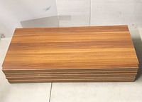 Stack of 8 wooden shelf boards with wood grain finish shown horizontally stacked.