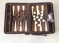 Open backgammon set showing playing board with brown and beige triangles, playing pieces in dark brown and ivory colors on the board, and a small plastic bag with dice and doubling cube.