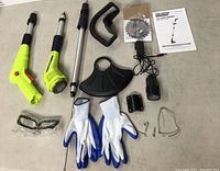 Photo of GardenJoy 12V lawn trimmer with motor unit, extension shaft, handle, blade guard, cutting blade, gloves, safety glasses, hardware, and manual on a flat surface.