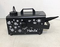 Side view of Hakuta snow machine showing black metal box decorated with white snowflakes, top handle, and nozzle output.