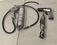 Photo showing all three air tools: pneumatic grease gun, pneumatic impact wrench, and pneumatic ratchet wrench laid on floor.