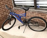 Side view of blue Mongoose Dynamic mountain bike showing full bike profile with knobby tires, suspension, and pedals.