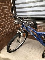 Close-up of front half of blue Nakamura Maya bicycle showing handlebars and front wheel with knobby tire.