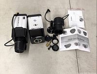 Top view of cameras and accessories spread on floor including two camera bodies, multiple lenses, mounting hardware, and manuals.