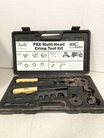 Opened plastic tool case showing PEX crimp tool with yellow handles and multiple rusted interchangeable heads inside.