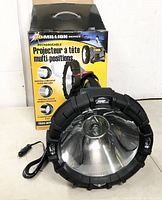 Front view of black rechargeable spotlight with large reflector head, handle, power cord, and packaging box in background showing product name and features.