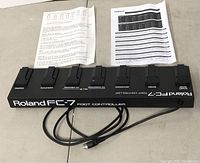 Roland FC-7 Foot Controller with cable and two instruction sheets placed on a flat surface.